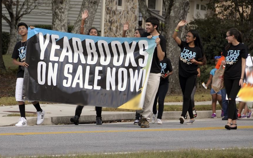 Picture of students in parade holding sign that says Yearbook on Sale Now. Picture of students in parade holding sign that says Yearbook on Sale Now.